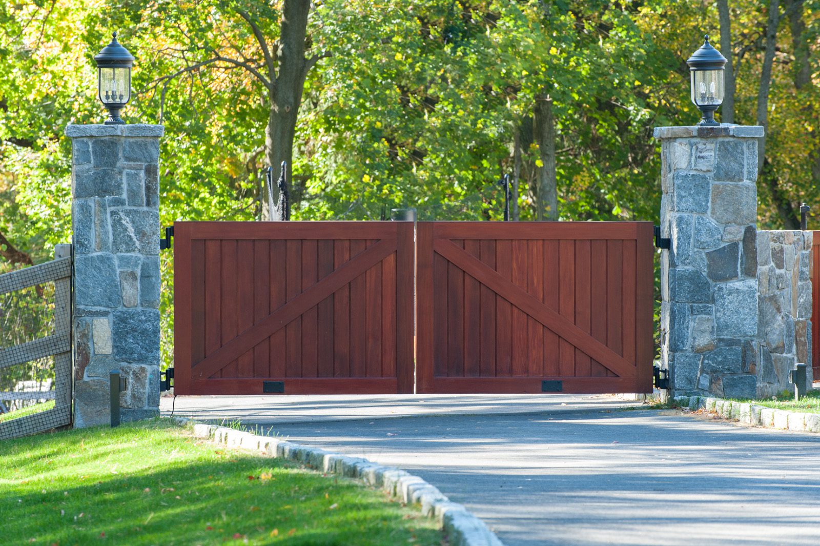 wooden driveway gate with large stone block pillars and lighting