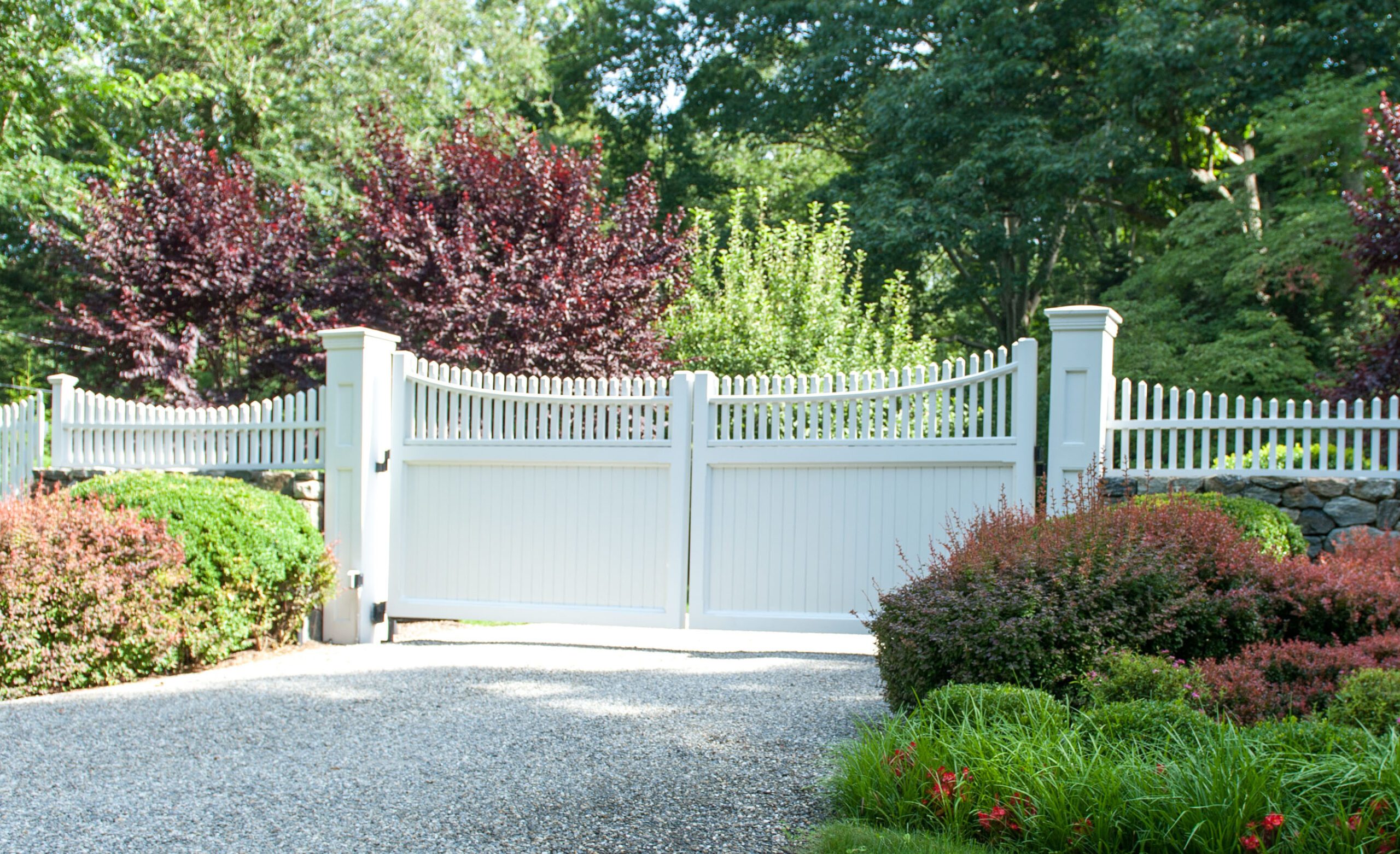 A large white composite swing gate with gently scalloped pickets above made to complement the surrounding fence.