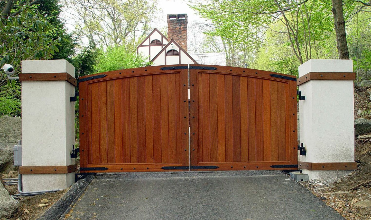 A rich, mahogany wood gate with metal trim along the panels between two tall white columns.