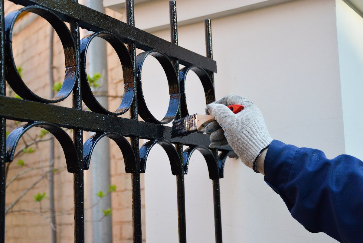 gloved hand painting a wrought iron gate for winter readiness