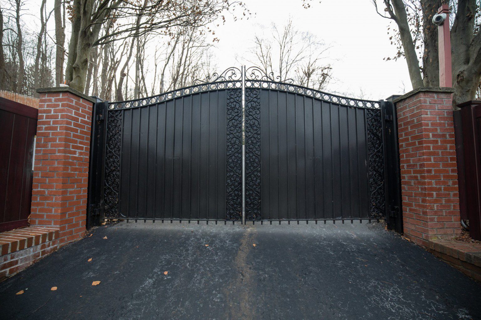 A black metal swing gate sits between brick columns.