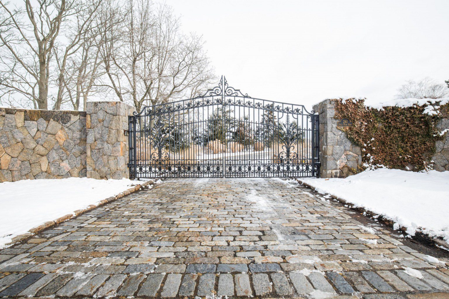 wrought iron driveway gate with stone pillars surrounded by snow