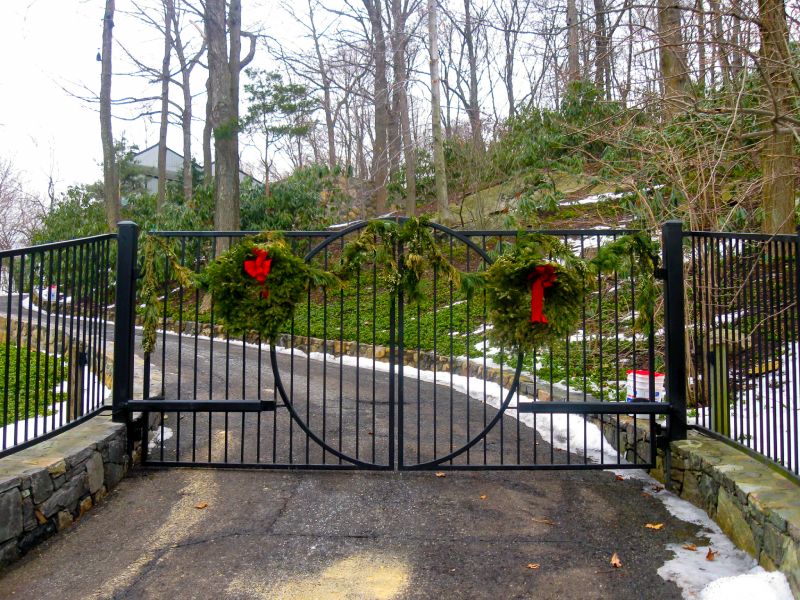 A Black Metal Gate with Circular Pattern and Decorated with Two Christmas Wreaths.