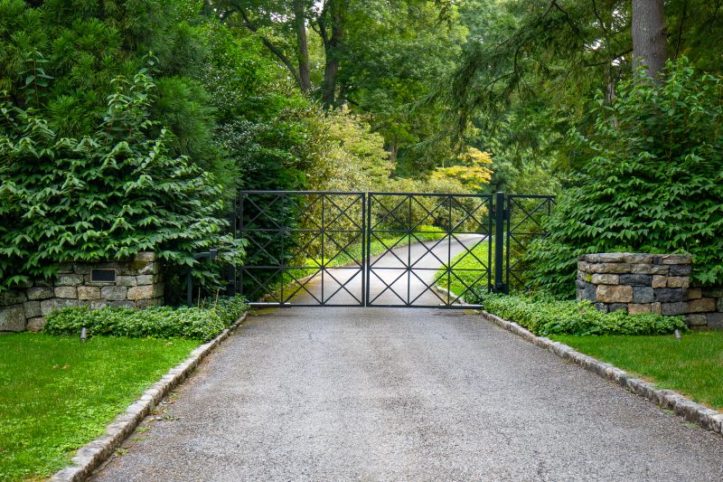 A Modern Gate Made Of Square Pickets Sits Between Two Large Shrubs