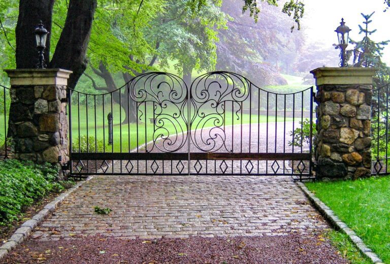 metal driveway gate with butterfly design and matching fencing with stone columns
