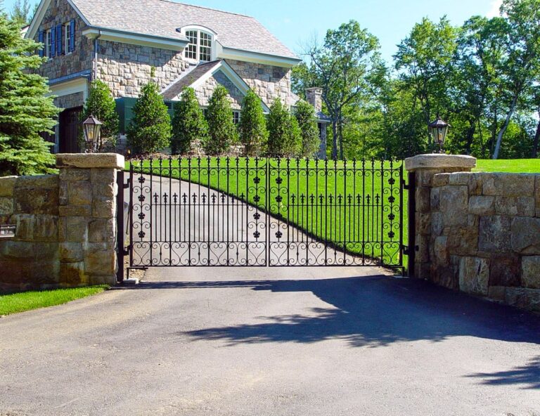 iron driveway gate with finials and sandstone colored stone fencing