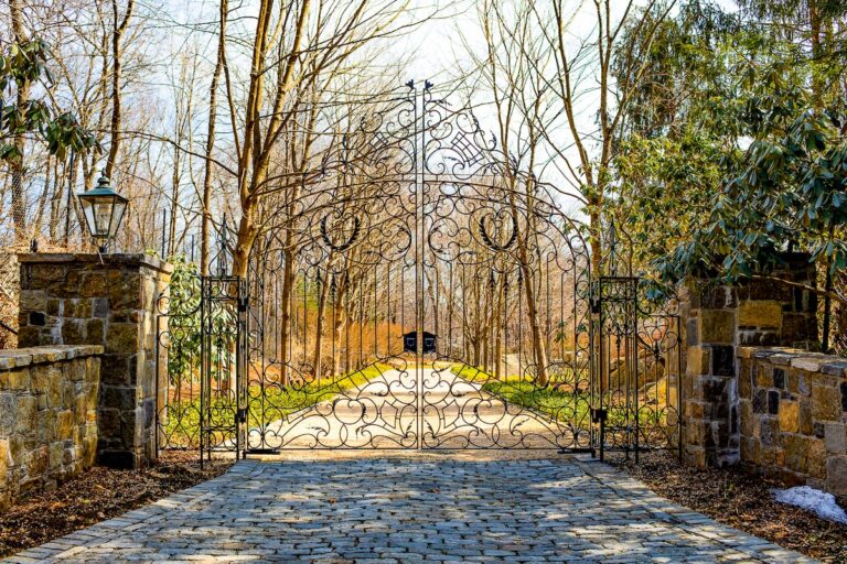 uniquely designed tall metal swing driveway gate with large stone columns and fencing