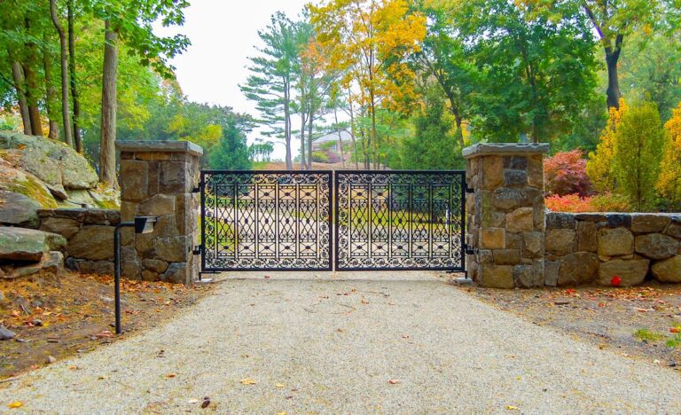 square metal swing driveway gate with unique cross and swirl patterns and large stone columns and fencing