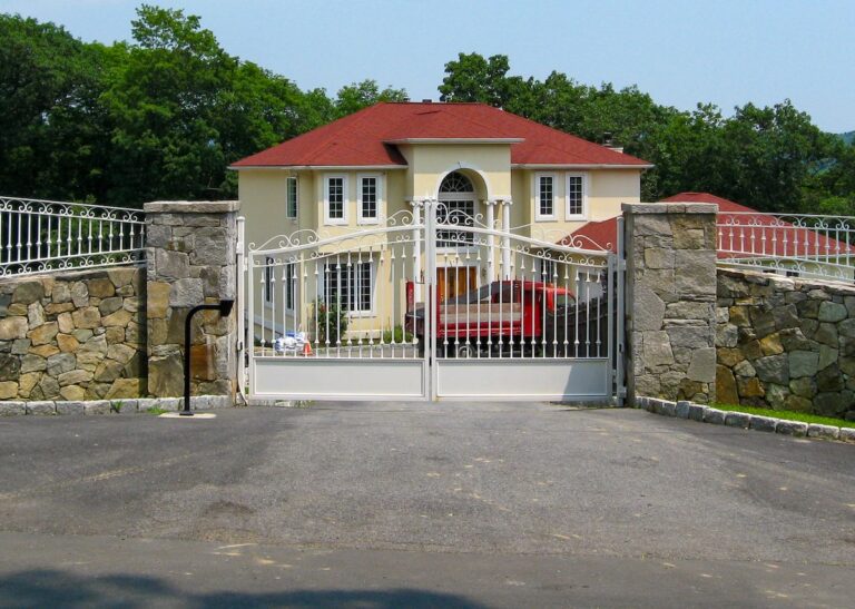 white metal driveway gate with stone pillars and fencing