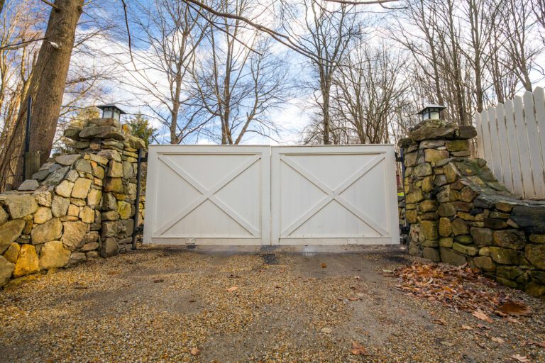 white barn style composite gate with natural stone fence
