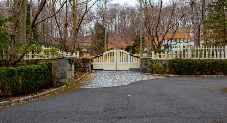beige arched driveway gate with black hardware and stone fence