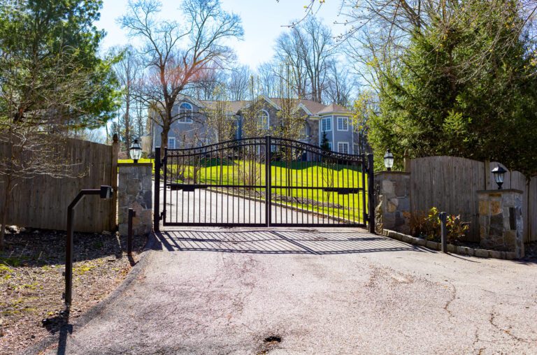 Metal driveway gate at the bottom of a hill with a house in the background
