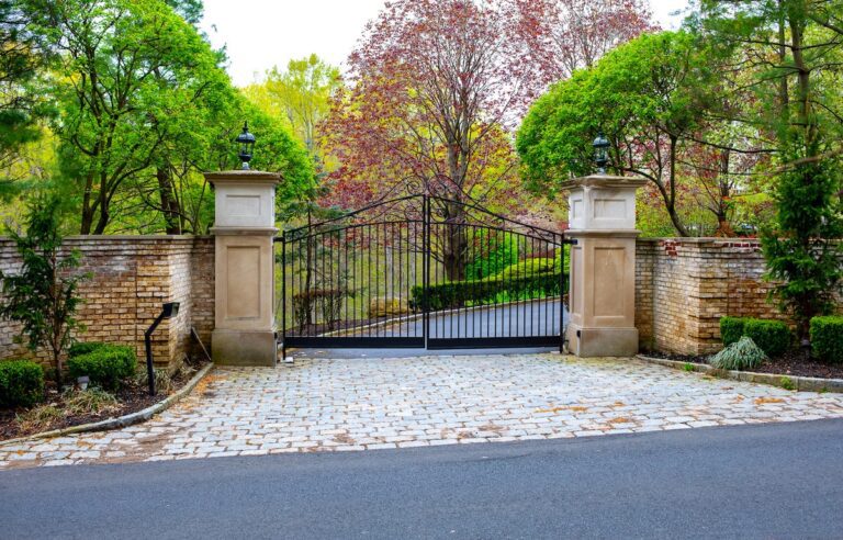 arched iron driveway gate with tall carved stone columns and lanterns