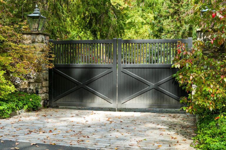 Tall black wooden driveway gate with post rail style design and lanterns on stone columns