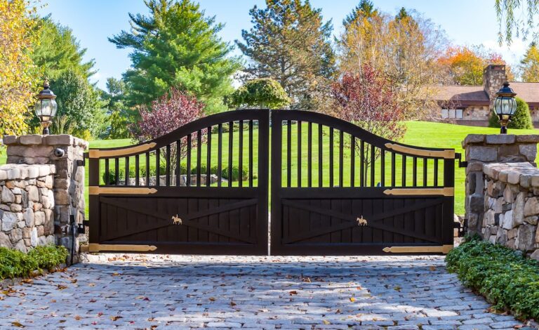 Arched black driveway gate with custom horse metal work and natural stone pillars and fencing