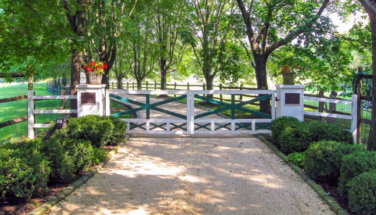 white wood swing gate with painted green cross design and wood columns with planters