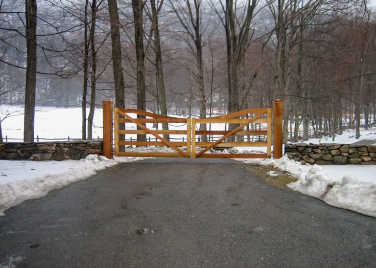 cedar farmhouse post rail swing gate with low stone fence in the snow