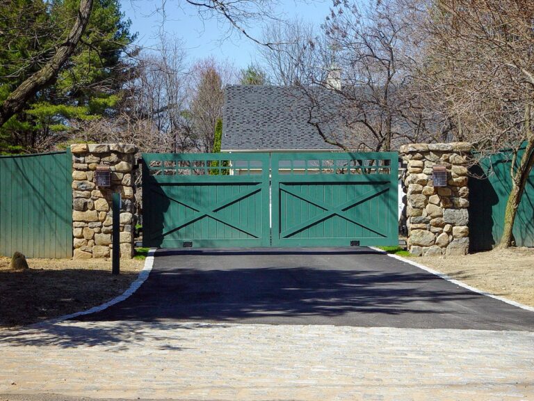 green barn style wooden driveway gate with post rail inspired cross design and stone columns