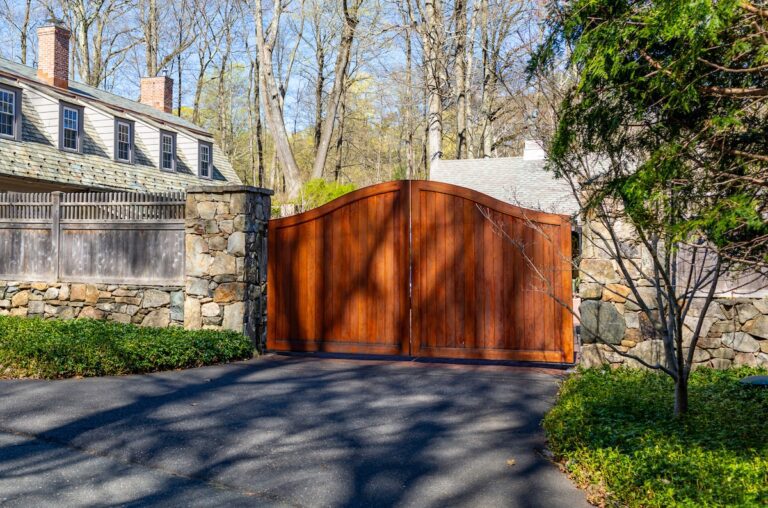 Arched mahogany swing gate with wood fence and stone apron