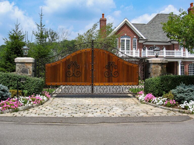 large dark wood driveway gate with metal frame and decor supported by stone pillars with lanterns
