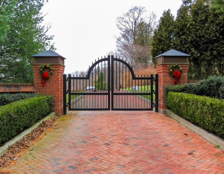 black wood driveway gate with prominent arch and brick columns decorated with wreaths