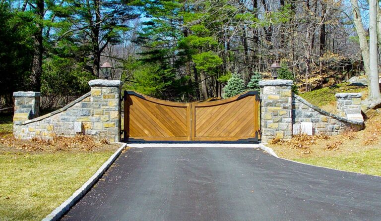 scalloped wood driveway gate with diagonal slats and stonework columns and sloping fence