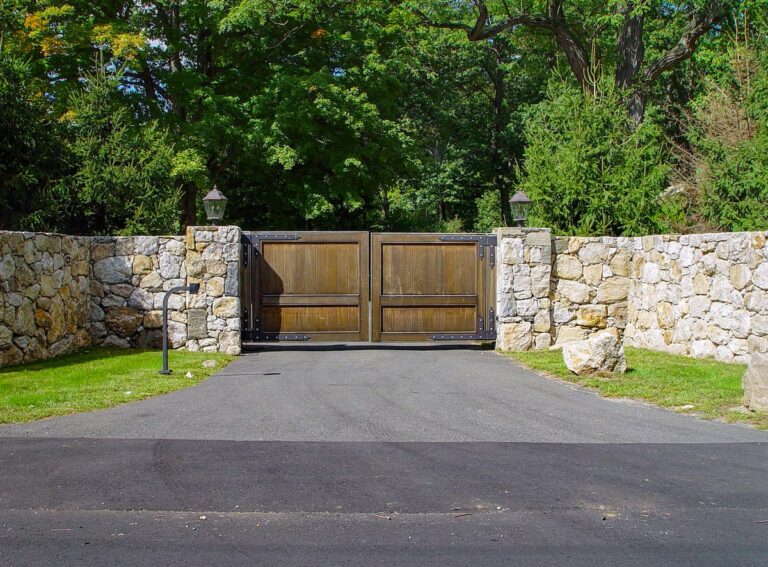 faded square wood driveway gate with black hardware and natural stone fence