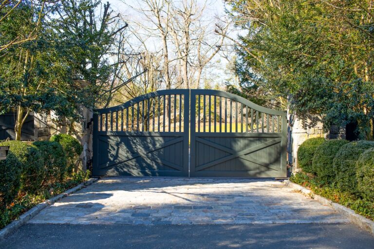 traditional tall arched green wooden driveway gate with hedges