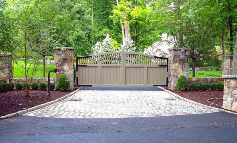 tan painted wood driveway gate with black hardware and low stone fence and columns