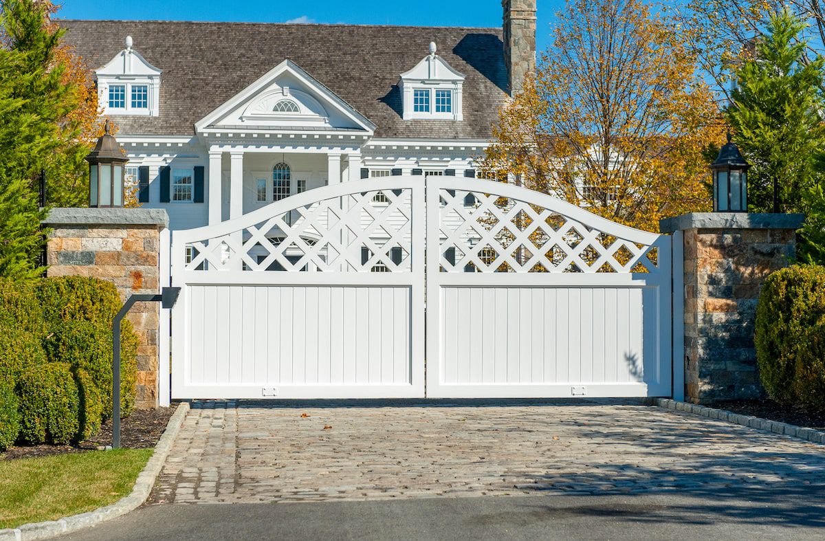 An automatic driveway gate made from white-painted wood complements the appearance of the home behind it.