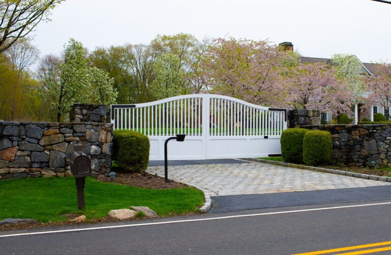 traditional arched white wooden driveway gate with stone pillars from the side view including keypad
